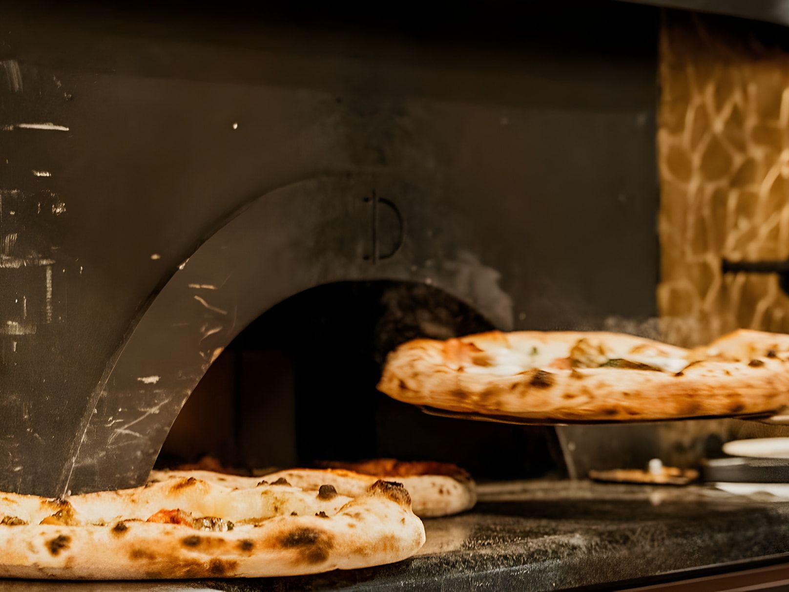 Goldener Mosaik-Kuppelofen der Pizzeria Capri: Eine Pizza kommt auf der Schaufel aus dem Ofen, zwei fertige Pizzen liegen davor