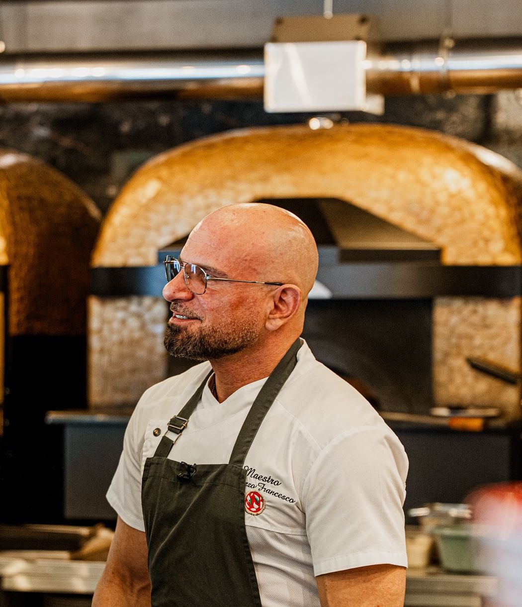 Francesco Ialazzo in Kochschürze vor den zwei goldenen Mosaik-Kuppelöfen der Pizzeria Capri