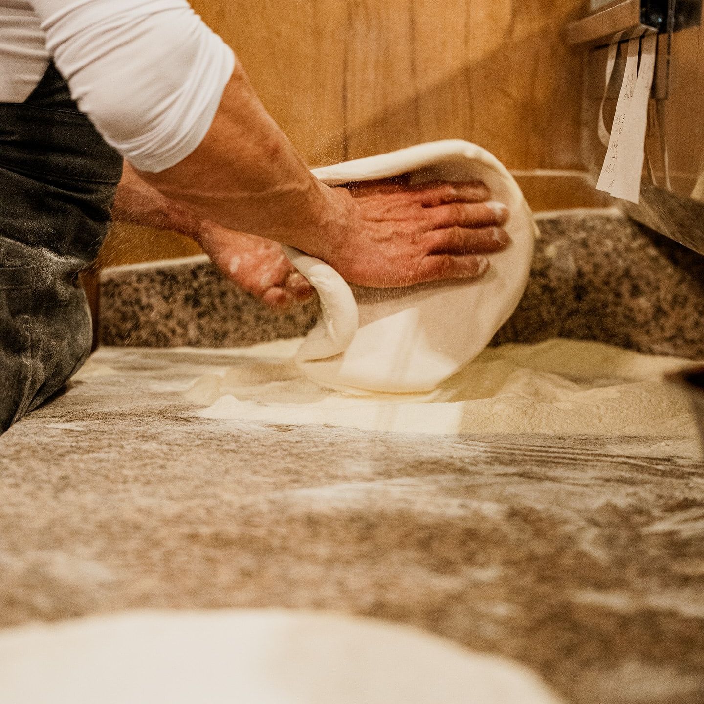 Hände formen auf bemehltem Granit einen Teigfladen