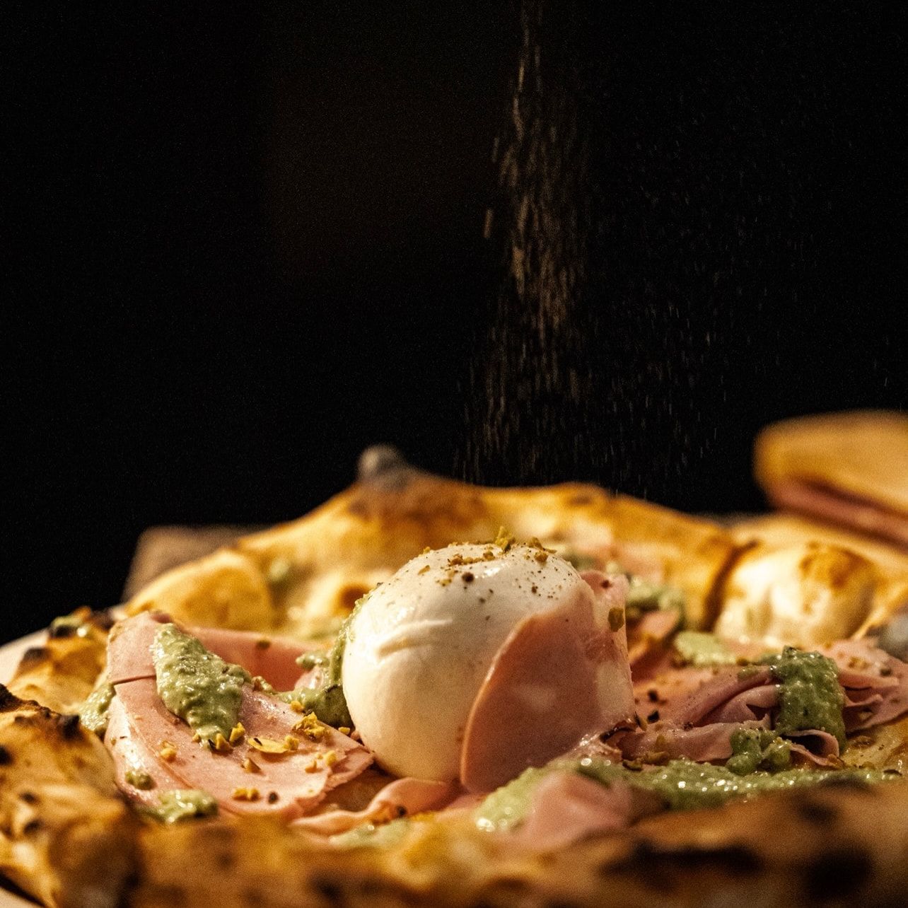 Pizza mit Mortadella, Burrata und Pistazien, von oben rieseln gehackte Pistazien
