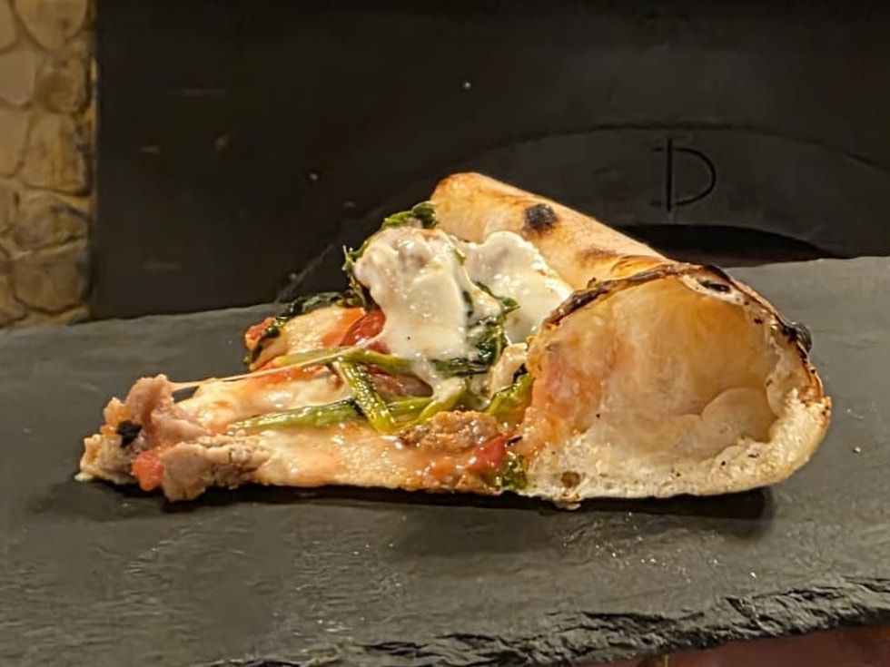 Ein Stück Pizza Sofia auf einer Schieferplatte vor dem Ofenmund